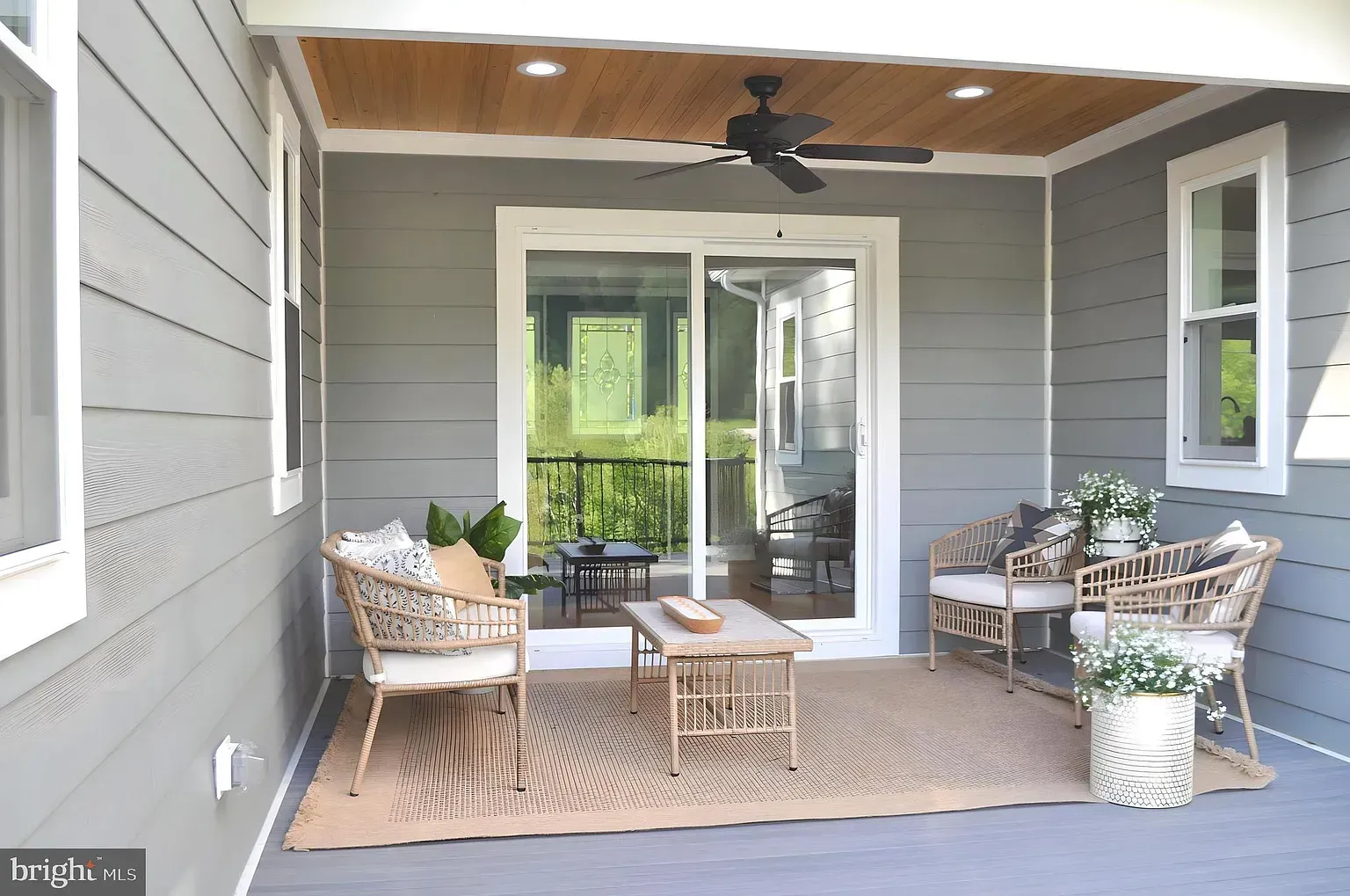 Covered patio with wicker furniture, sliding glass door, and wooden ceiling. Grey siding.