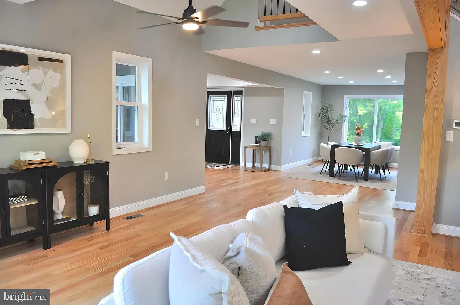 Living room with hardwood floors, white couch, black accent furniture, and dining area.