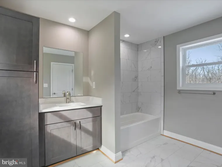 Bathroom with gray cabinets, white countertop, and tiled shower. Window on the right.