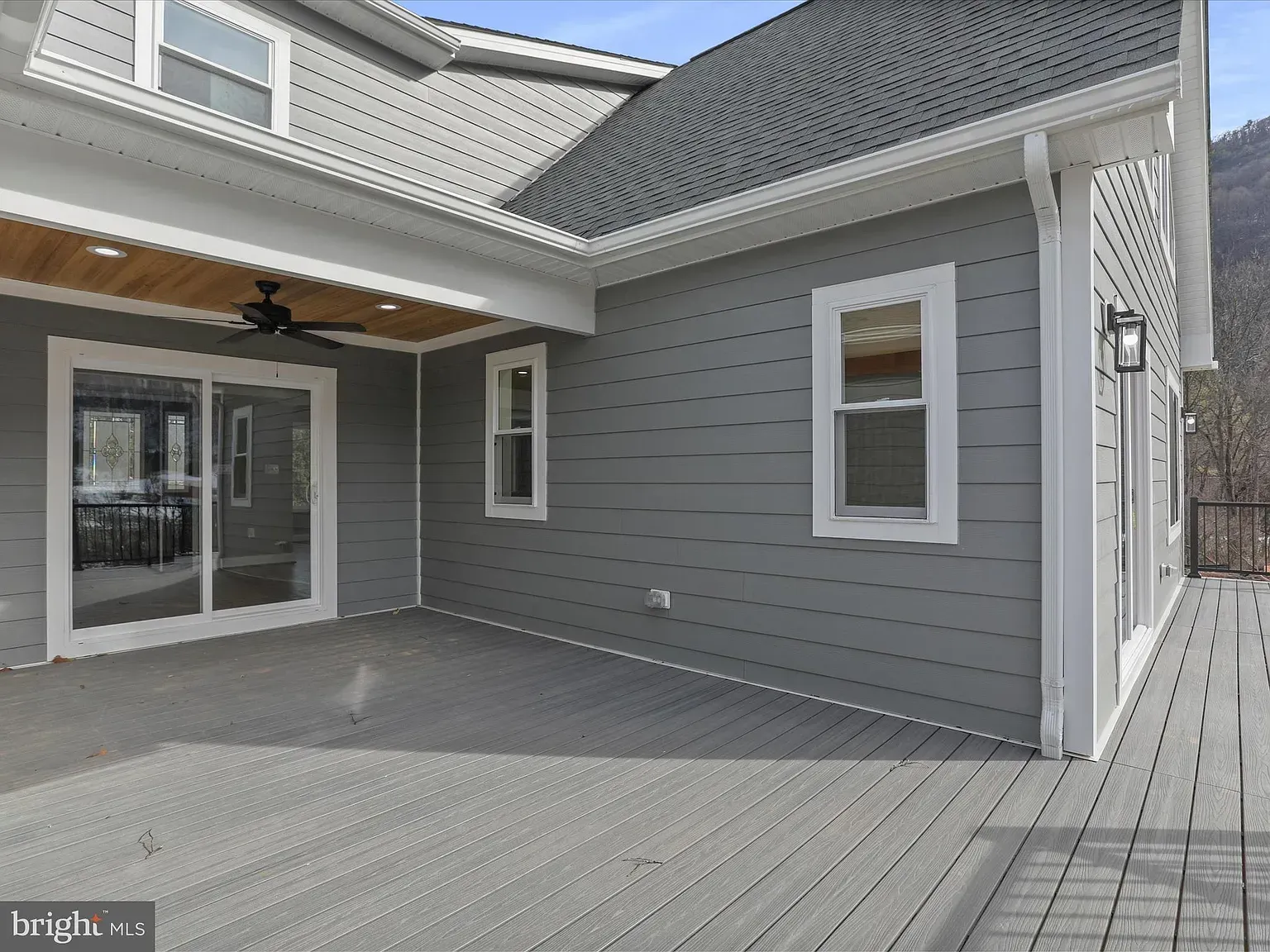 Gray house exterior with deck. Sliding glass door, windows, and light fixtures.