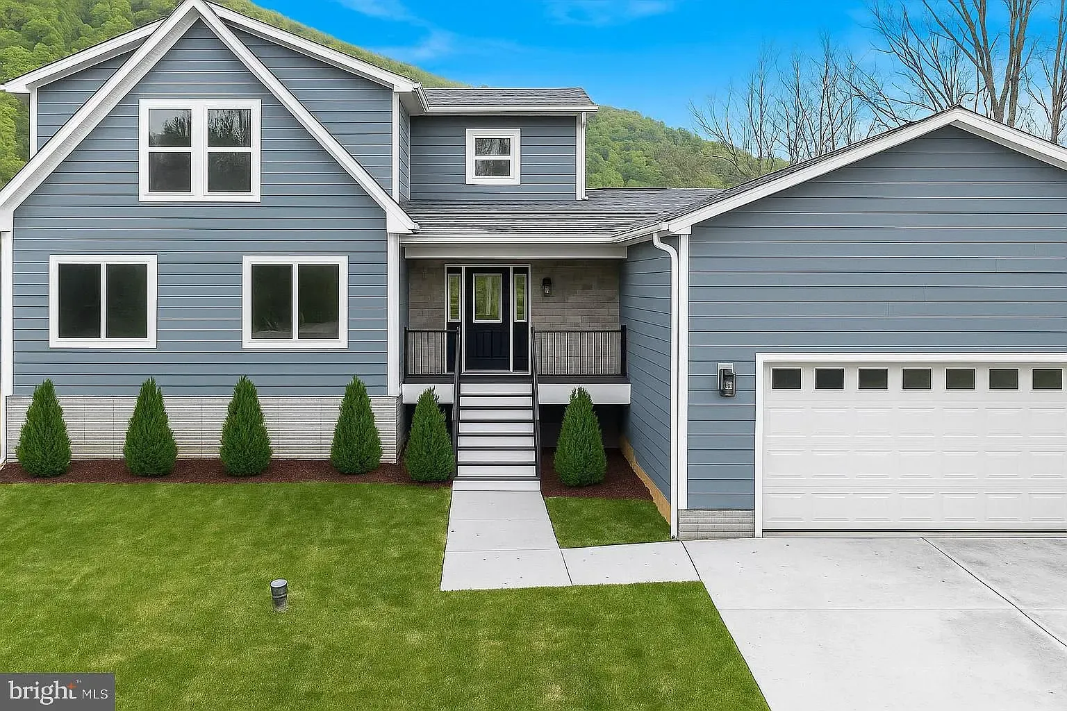 Blue house with attached garage, steps to entrance, green lawn.