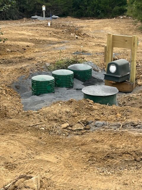 Green septic tanks and pump system in a dirt clearing.