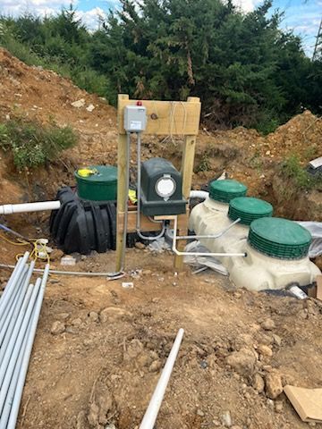 Construction site with a septic system, including tanks, piping, electrical components, and controls. Earthmoving in a natural outdoor setting.