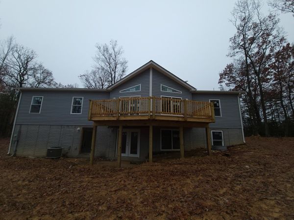 Gray house with a large wooden deck. Bare trees in the background, cloudy sky.