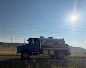 Blue utility truck parked on a rural roadside under a bright sun, with wind turbines in the distance