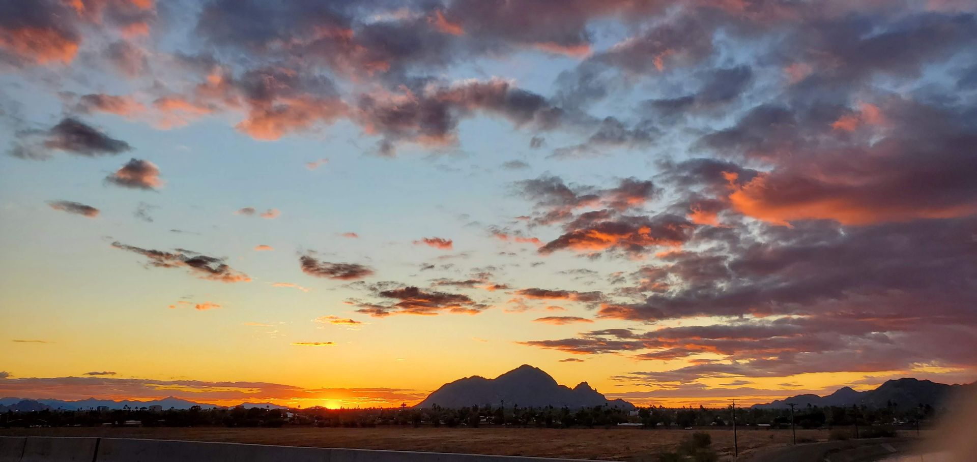 Sunset sky with orange, pink, and blue hues. A silhouette of mountains and desert landscape are visible.