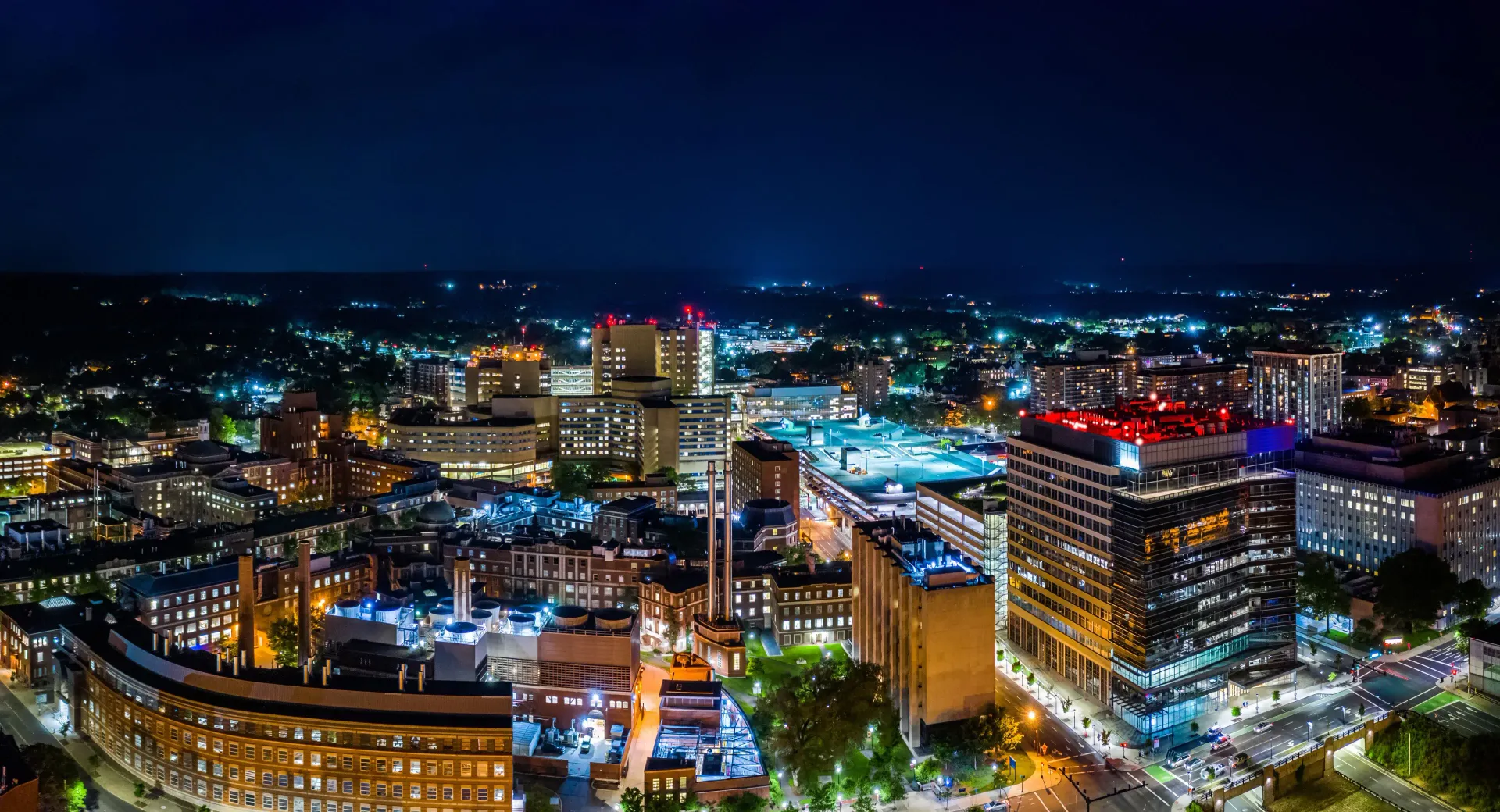 Nighttime city skyline with brightly lit buildings, streets, and a glowing urban center.