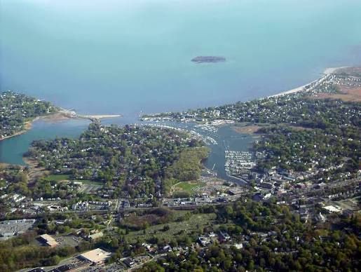 Aerial view of a coastal town with a bay, hillside homes, and a small island in the distance.