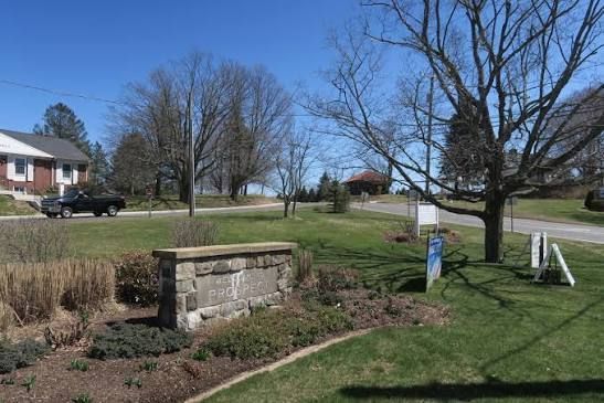 Stone garden sign in a grassy neighborhood park on a sunny day, with trees and houses in the background