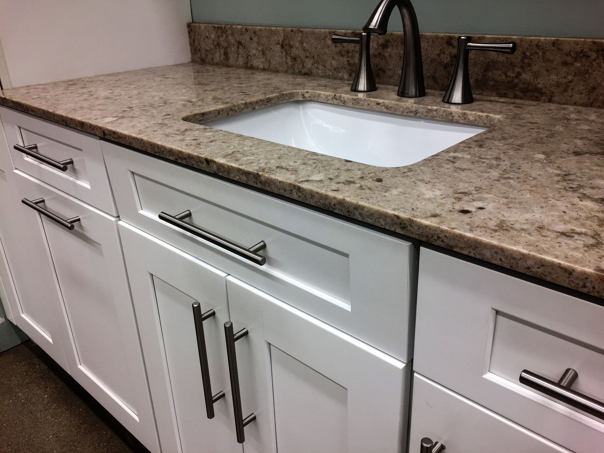 Modern white bathroom vanity with speckled countertop and integrated sink, chrome faucets, and cabinet drawers.