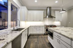 Bright modern kitchen with white cabinets, granite counters, stainless range hood, and large window over sink.
