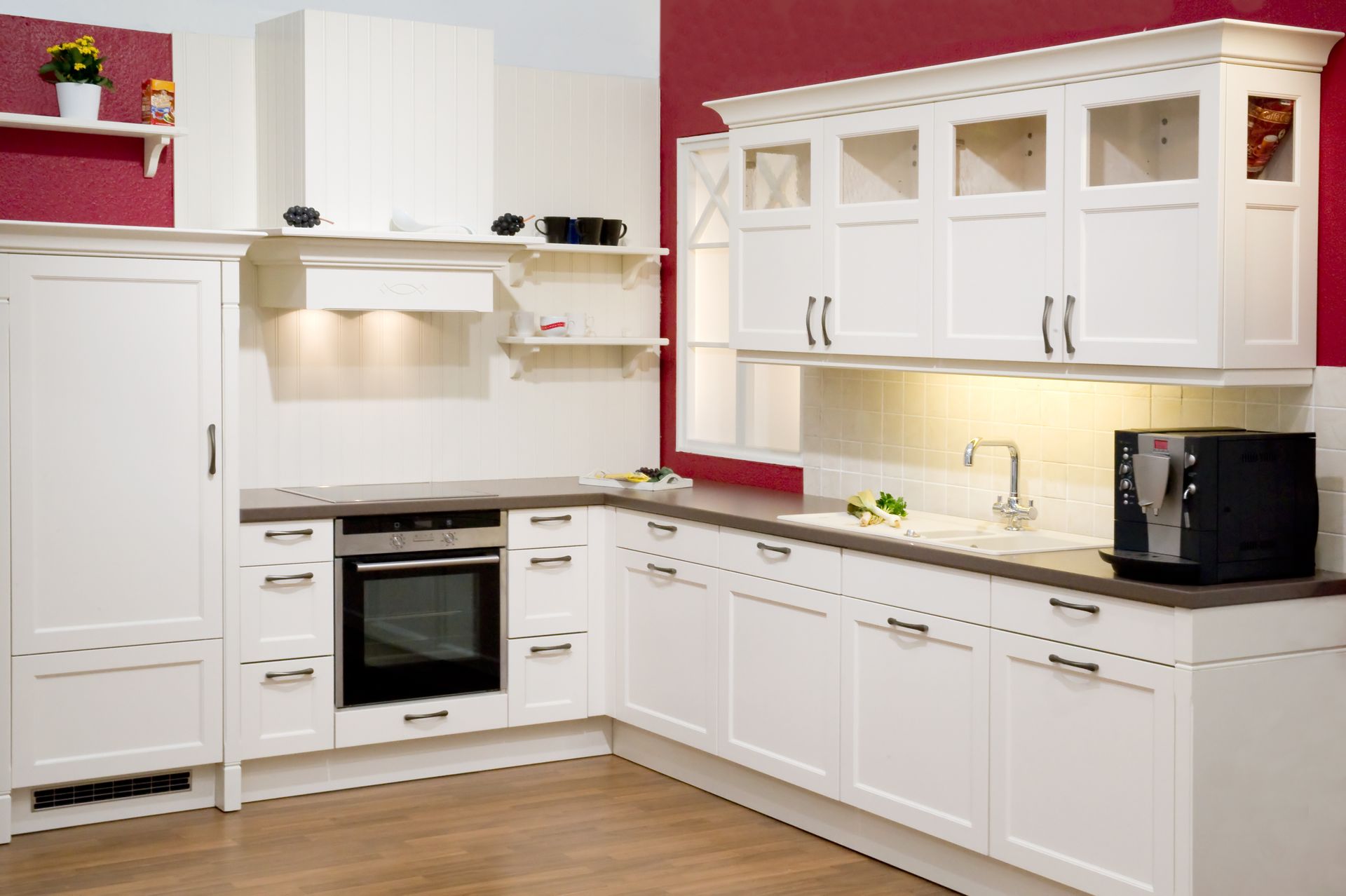 Bright white modern kitchen with cabinets, oven, black countertops, and light wood floor.