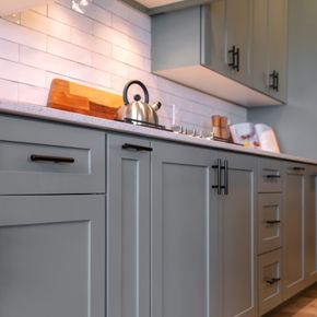 Modern gray kitchen cabinets with white subway tile backsplash and a kettle on the counter.