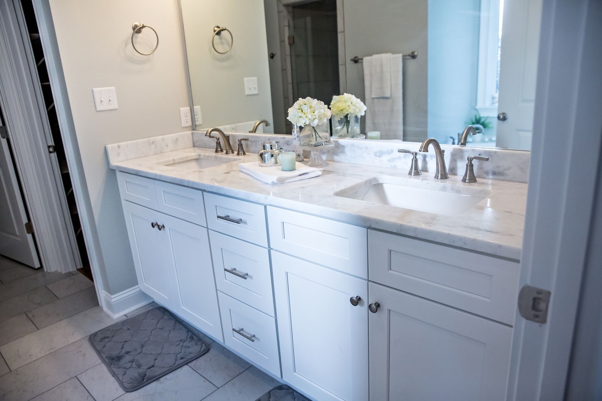 Bright bathroom vanity with white cabinets, marble countertop, double sinks, and large mirror.