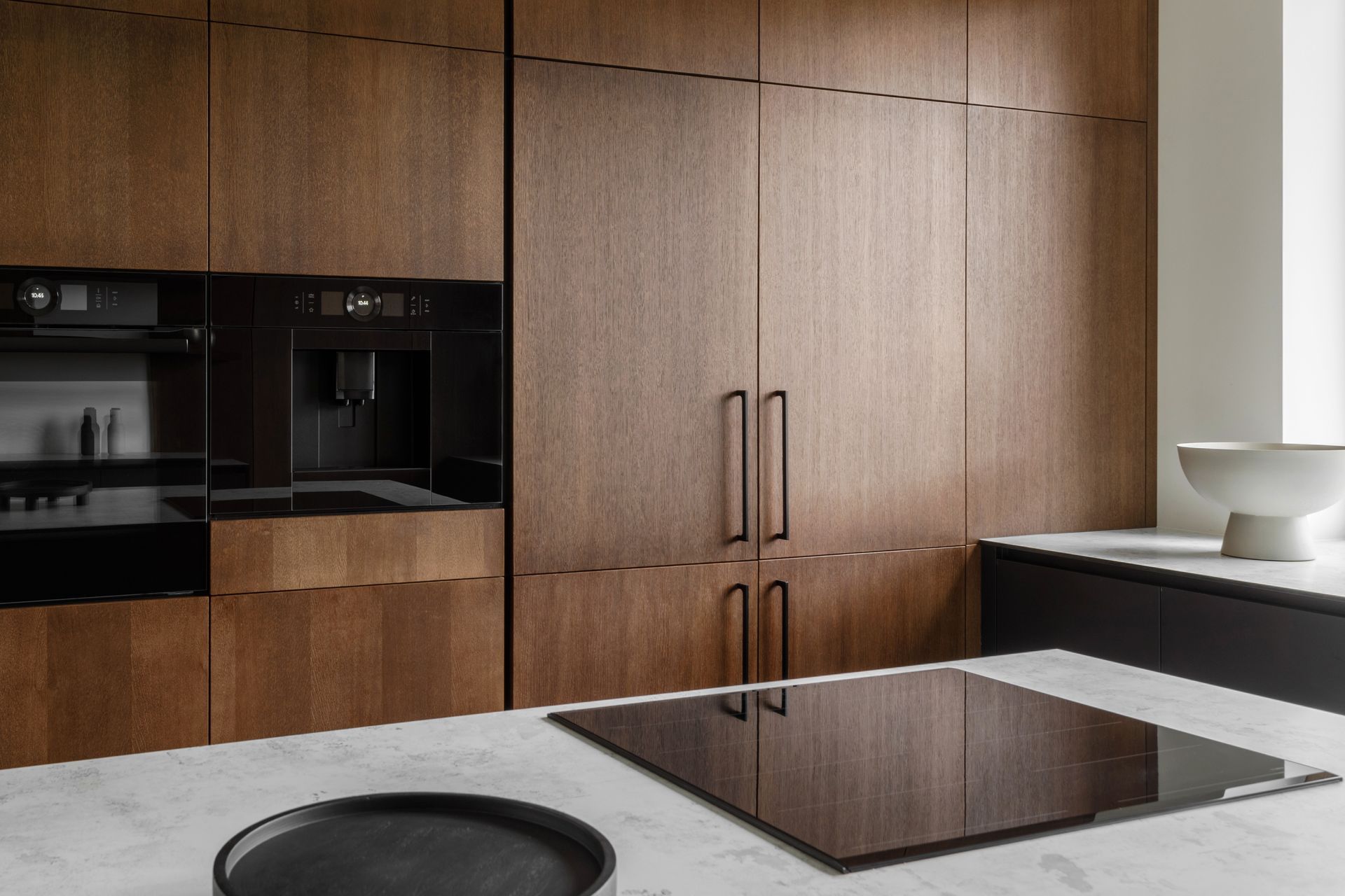 Modern kitchen with wood cabinets, built-in oven, and marble island with cooktop.