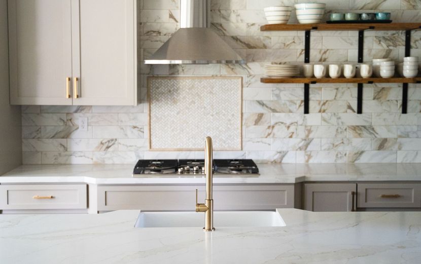 Modern white kitchen with marble backsplash, gold faucet, and open shelves of dishes. Modern white kitchen with marble backsplash, gold faucet, and open shelves of dishes.