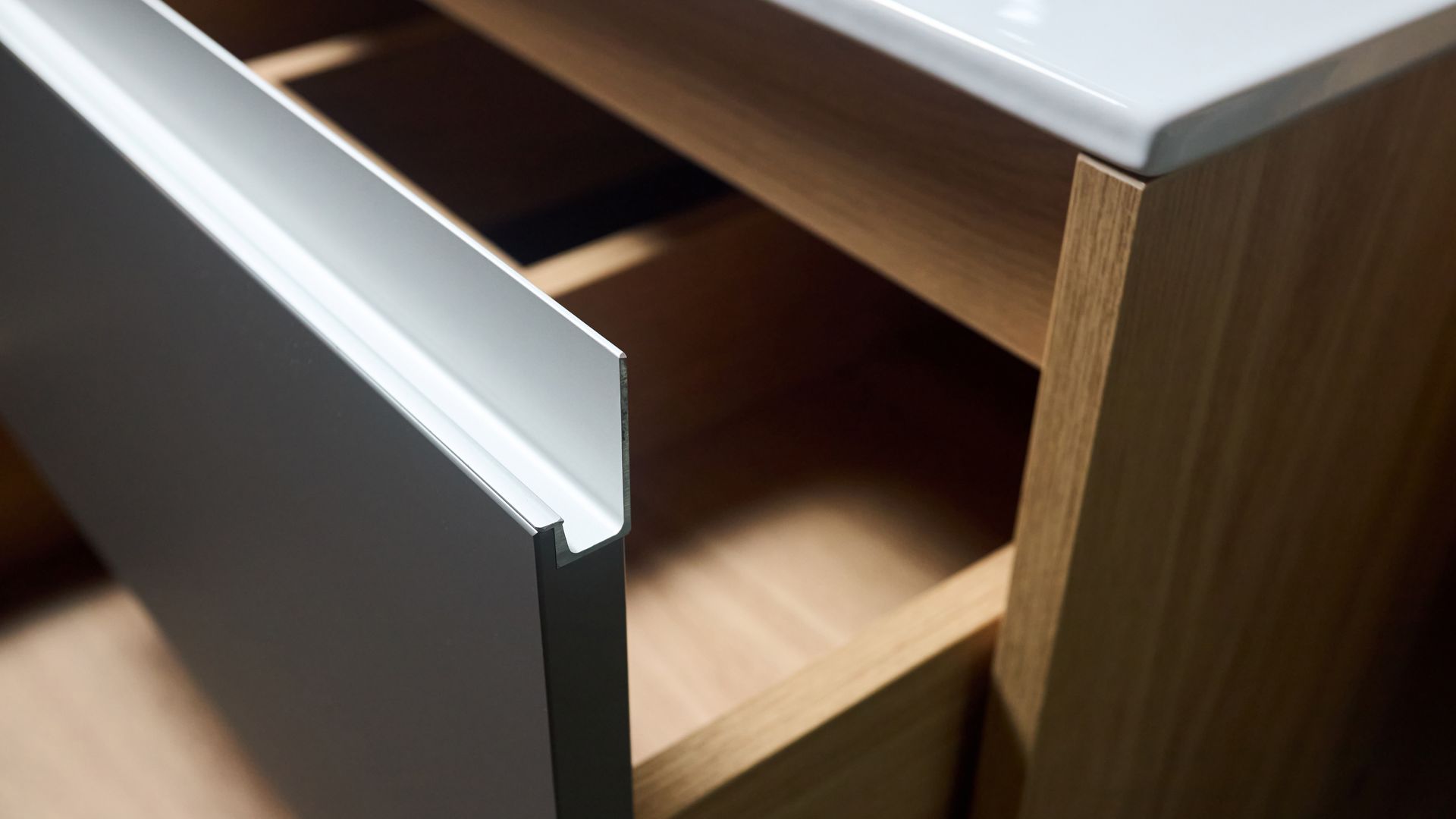 Partially open dark cabinet drawer with a light wood interior and silver handle. Partially open dark cabinet drawer with a light wood interior and silver handle.