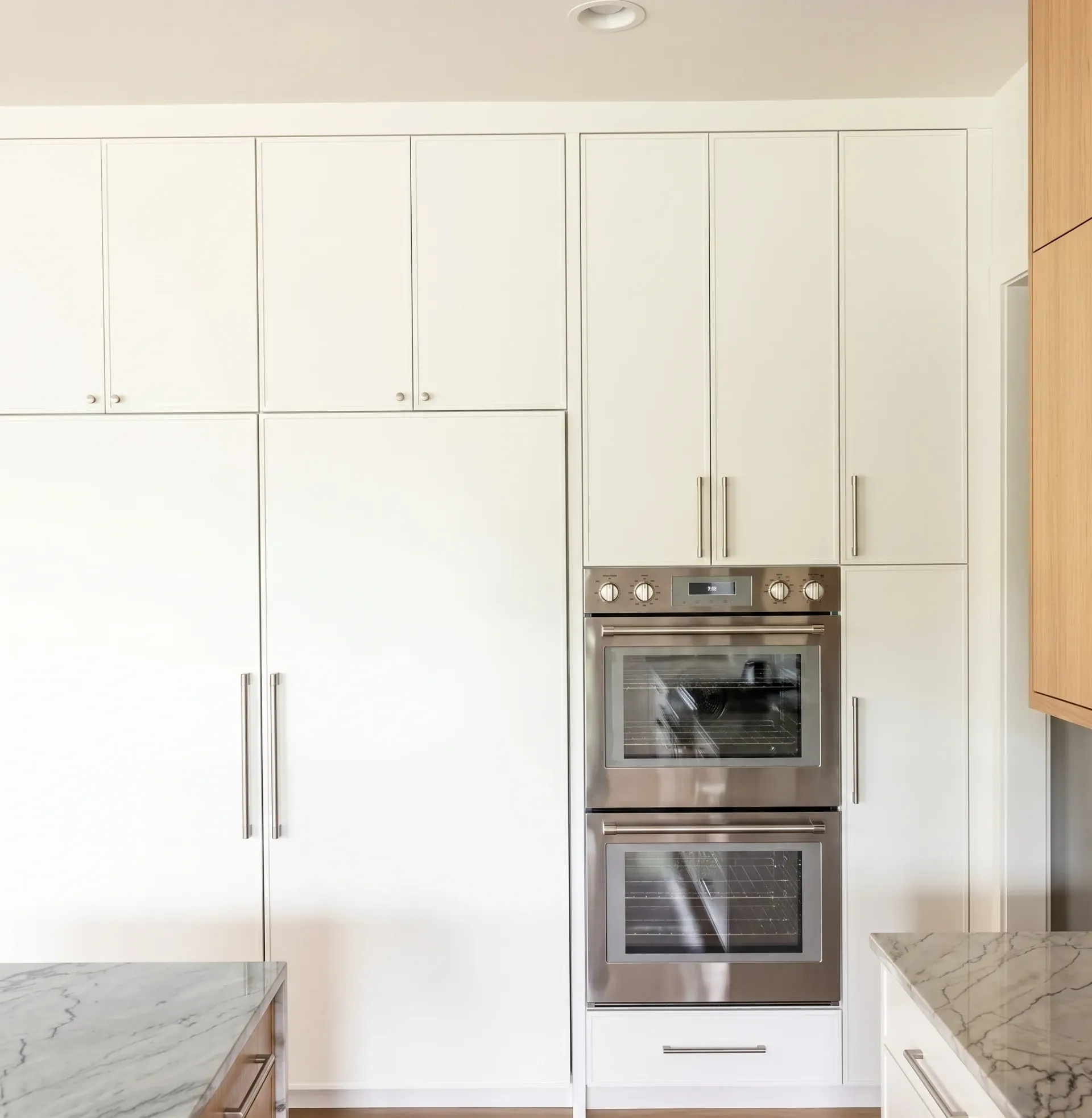 Modern white kitchen with built-in double oven and tall cabinets.