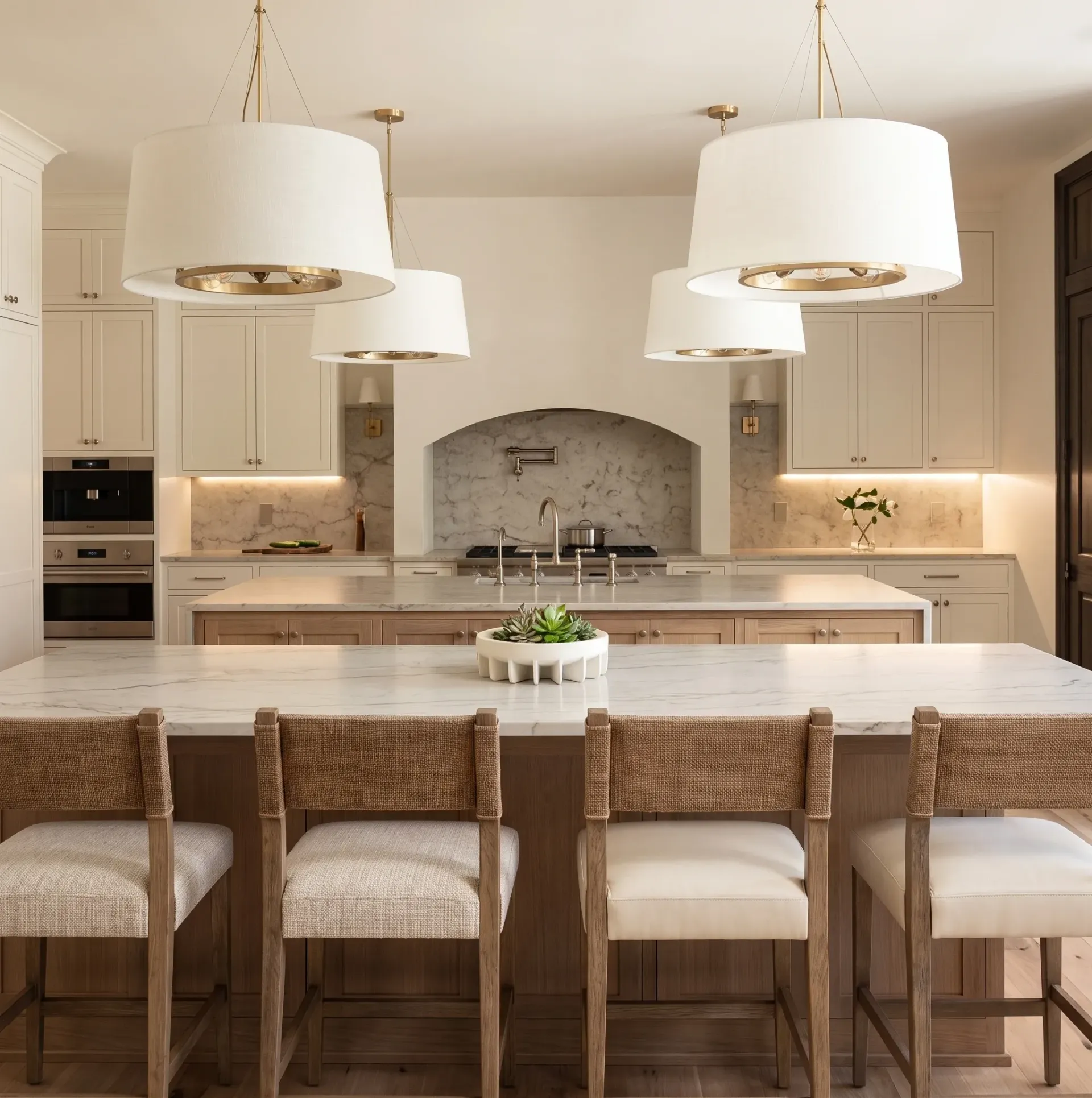Bright modern kitchen with large island, woven stools, pendant lights, and a stone arch backsplash.