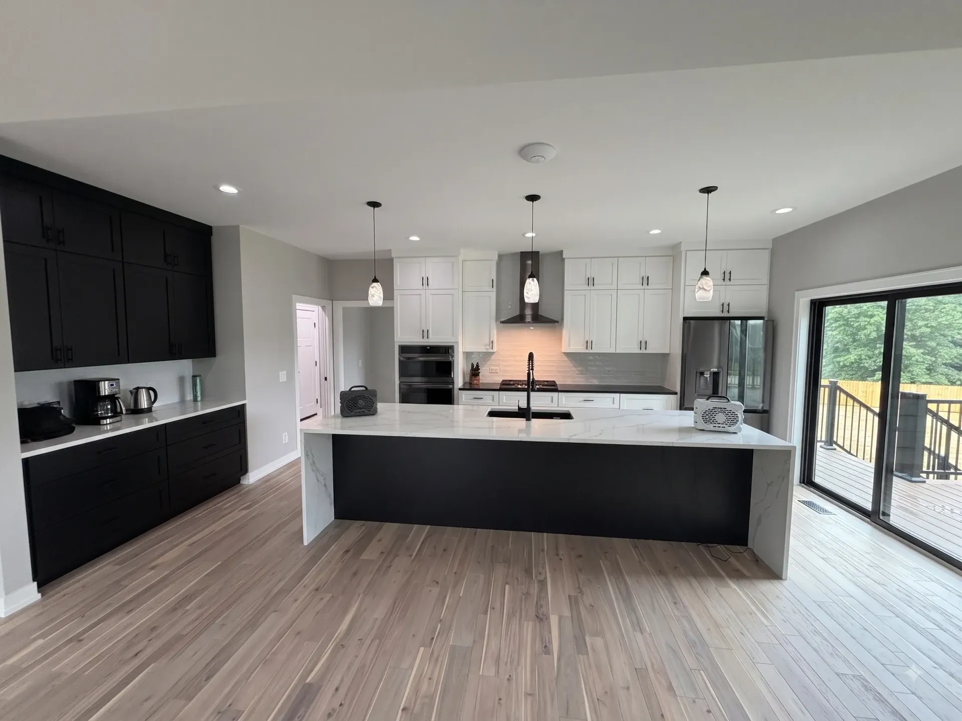Modern open-plan kitchen with black and white cabinets, island, wood floors, and sliding glass doors.