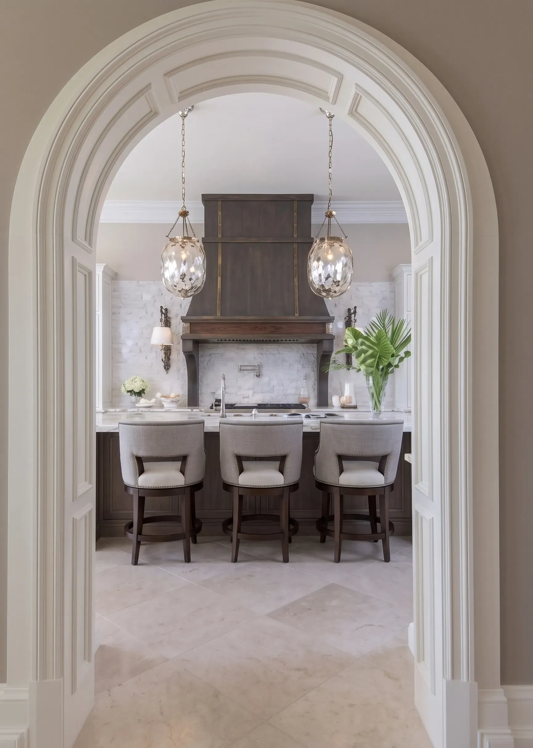 Elegant dining nook viewed through a white arched doorway, with three chairs, chandelier lights, and a mantel.