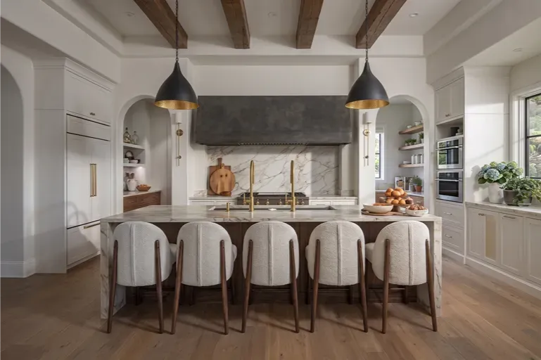 Bright modern kitchen with large island, six upholstered stools, and pendant lights.