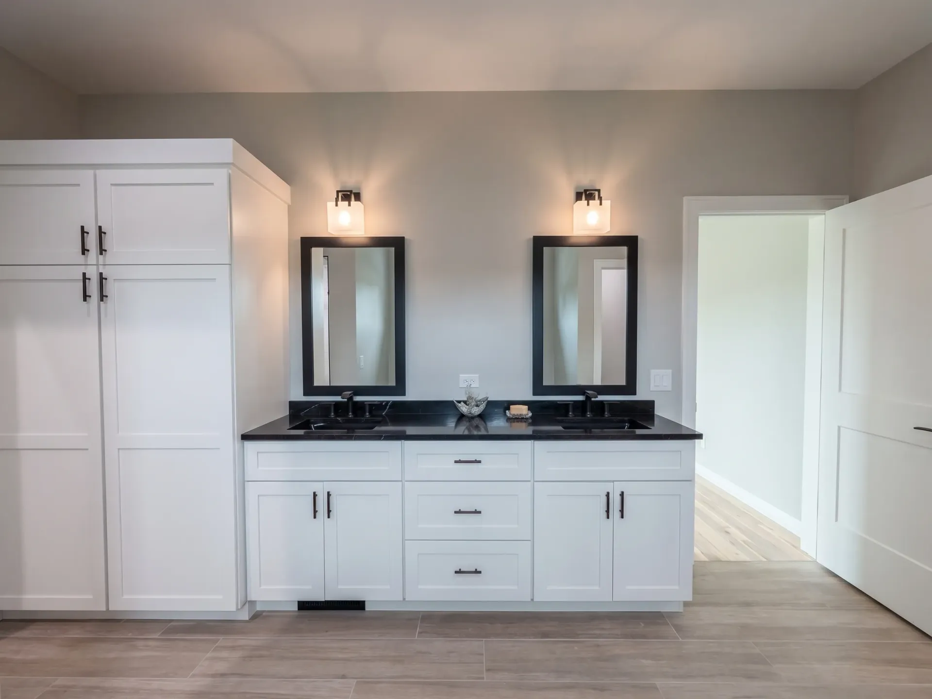 Modern double vanity bathroom with white cabinets, black countertop, and twin mirrors under wall sconces.