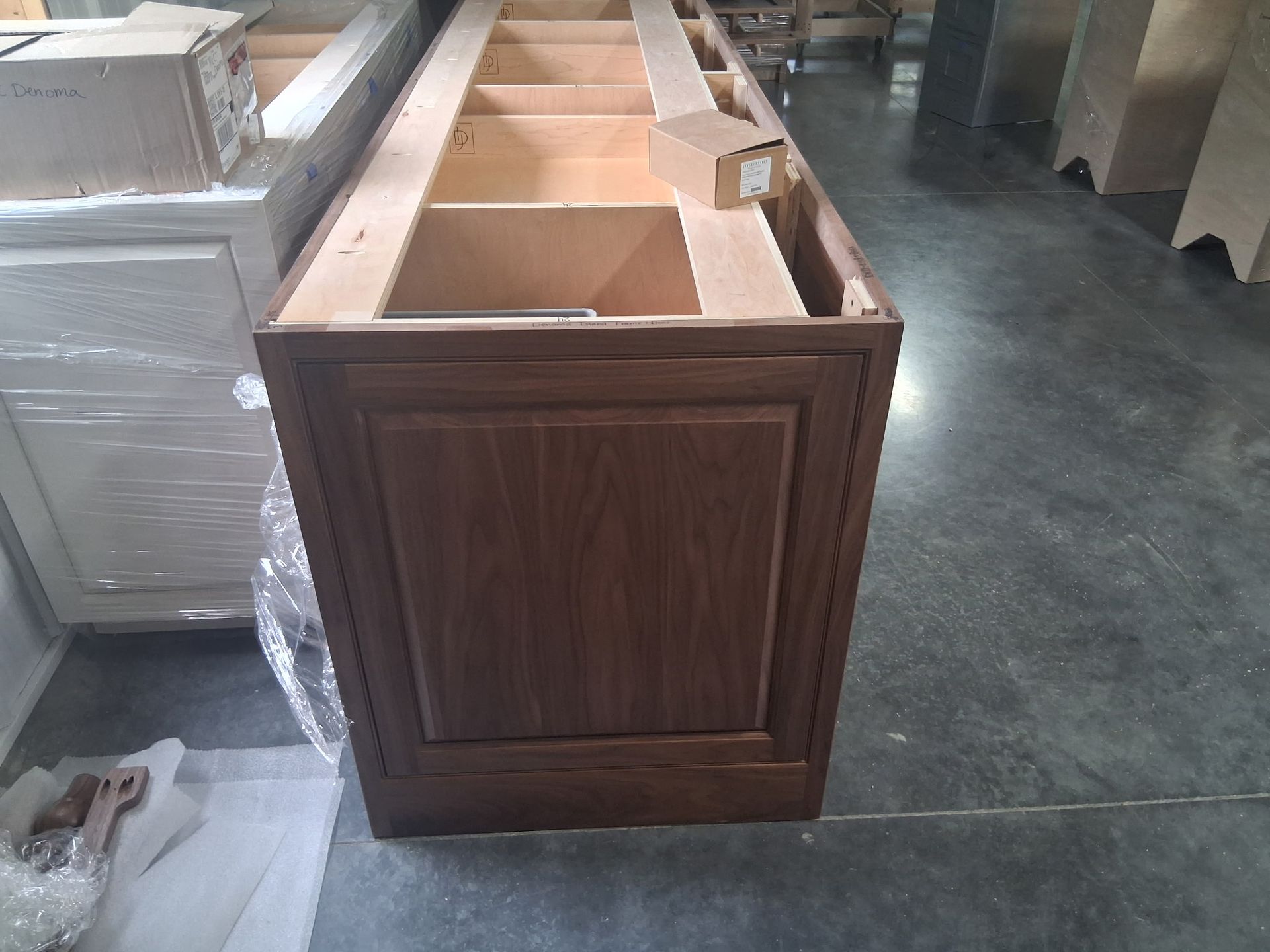 Wooden cabinet base with open compartments in a workshop or warehouse setting.