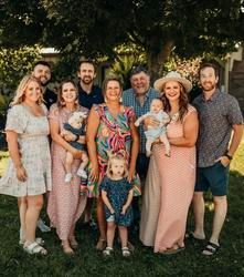 Group of eight people standing outdoors in a garden, smiling and posing together, with two children in front.