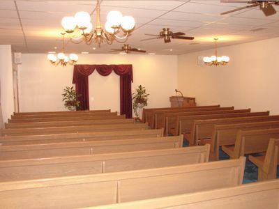 Empty church sanctuary with wooden pews, chandeliers, and a curtained pulpit at the front