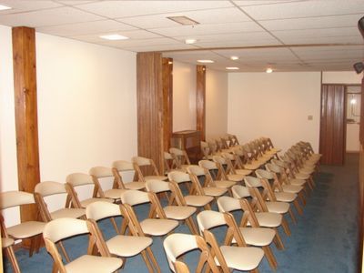 Rows of empty beige chairs in a carpeted conference room with wood columns and white ceiling panels
