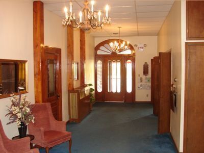 Hotel lobby hallway with chandelier, blue carpet, and a wooden front door with glass panes