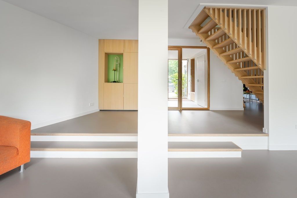Minimalistisch interieur met een trap, een witte pilaar, een oranje bank en een deuropening met een groen paneel.