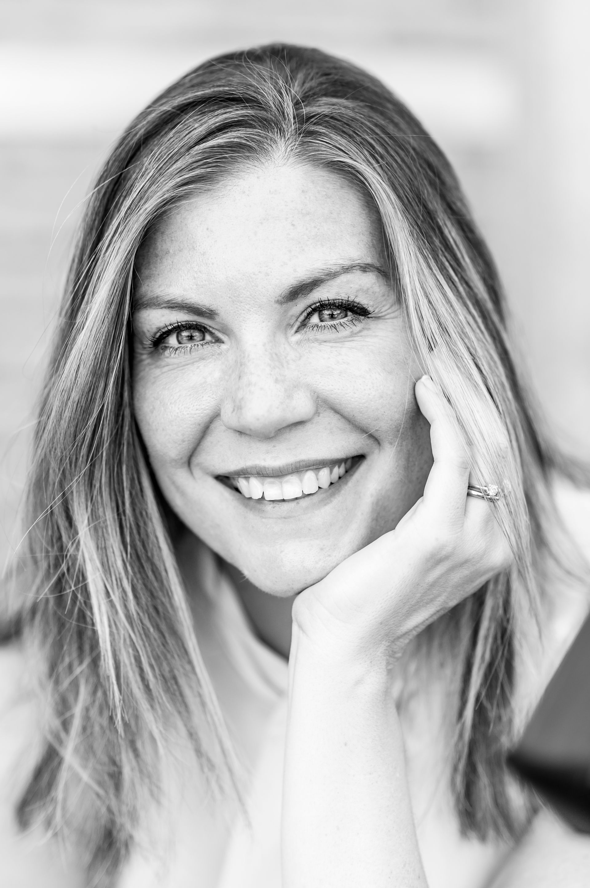 Lachende vrouw met steil haar die haar gezicht in haar hand laat rusten, in zwart-wit.