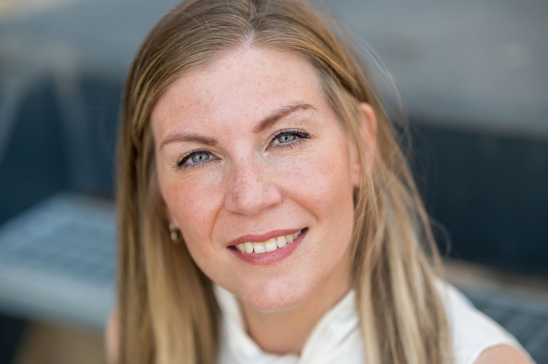 Portret van een lachende blonde vrouw in de buitenlucht met een wazige achtergrond.