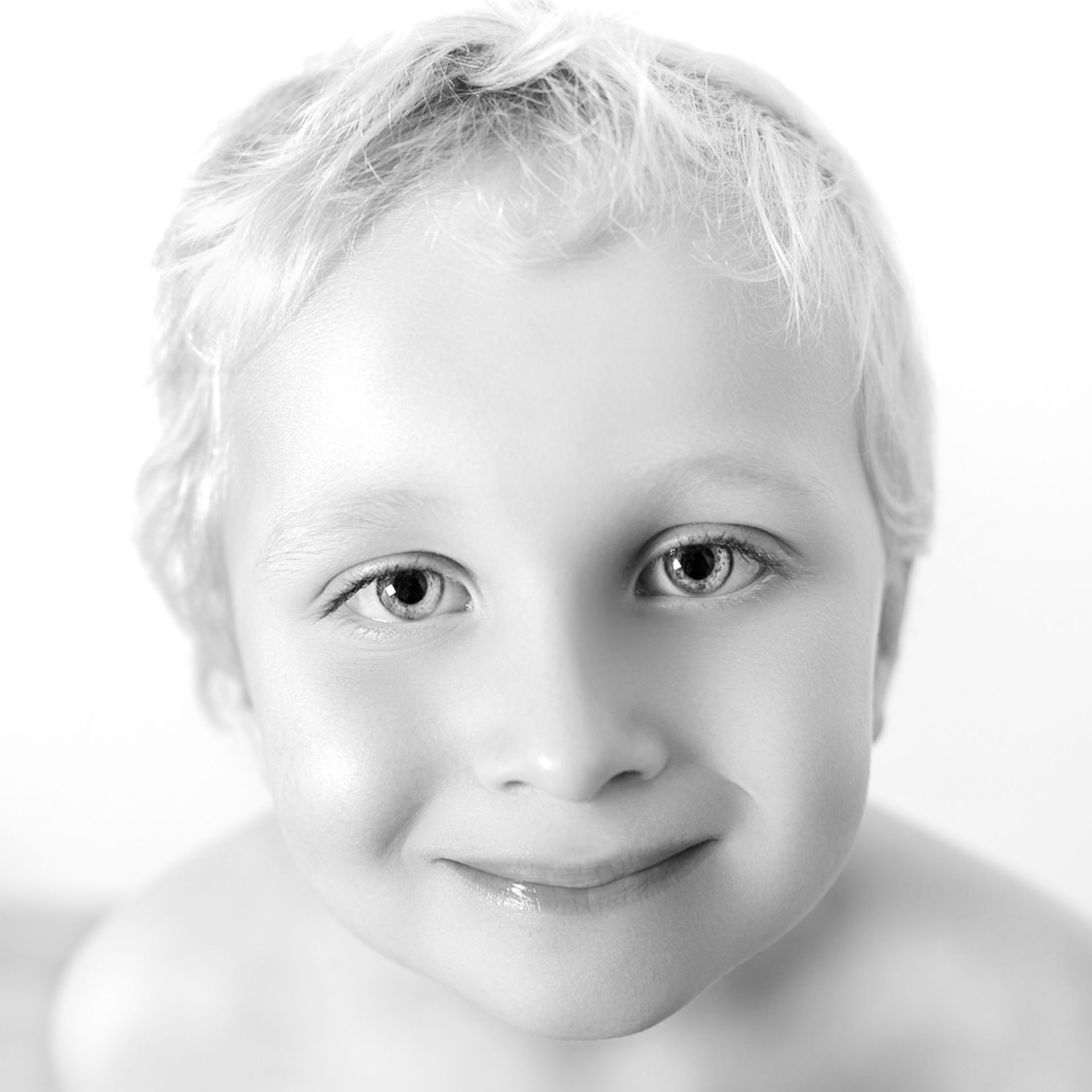 Close-up portret van een lachend kind met licht haar tegen een witte achtergrond.