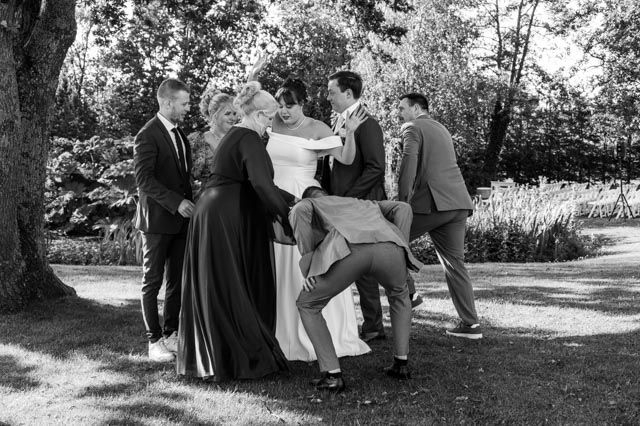 Het bruidspaar danst buiten op een gazon, terwijl de gasten in galakleding lachen en elkaar omhelzen.