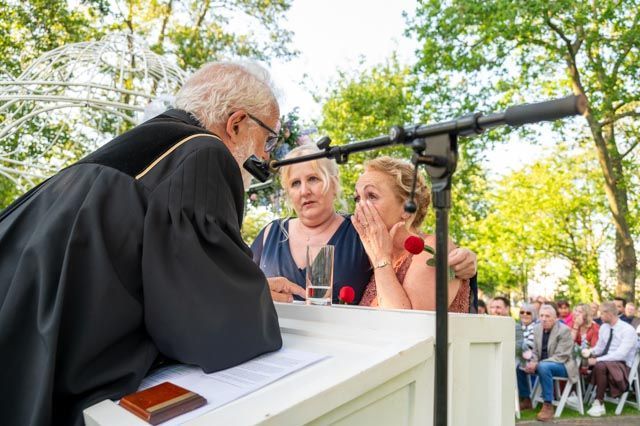Bruid en bruidegroom in gesprek met een ambtenaar van de burgerlijke stand tijdens een huwelijksceremonie in de buitenlucht.