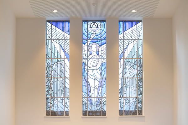 Drieluik van gebrandschilderd glas met blauw-witte abstracte figuren in een lichte gang.