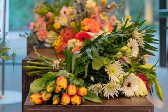 Boeketten met oranje en witte bloemen op een tafel, met een wazige bloemenpracht op de achtergrond.