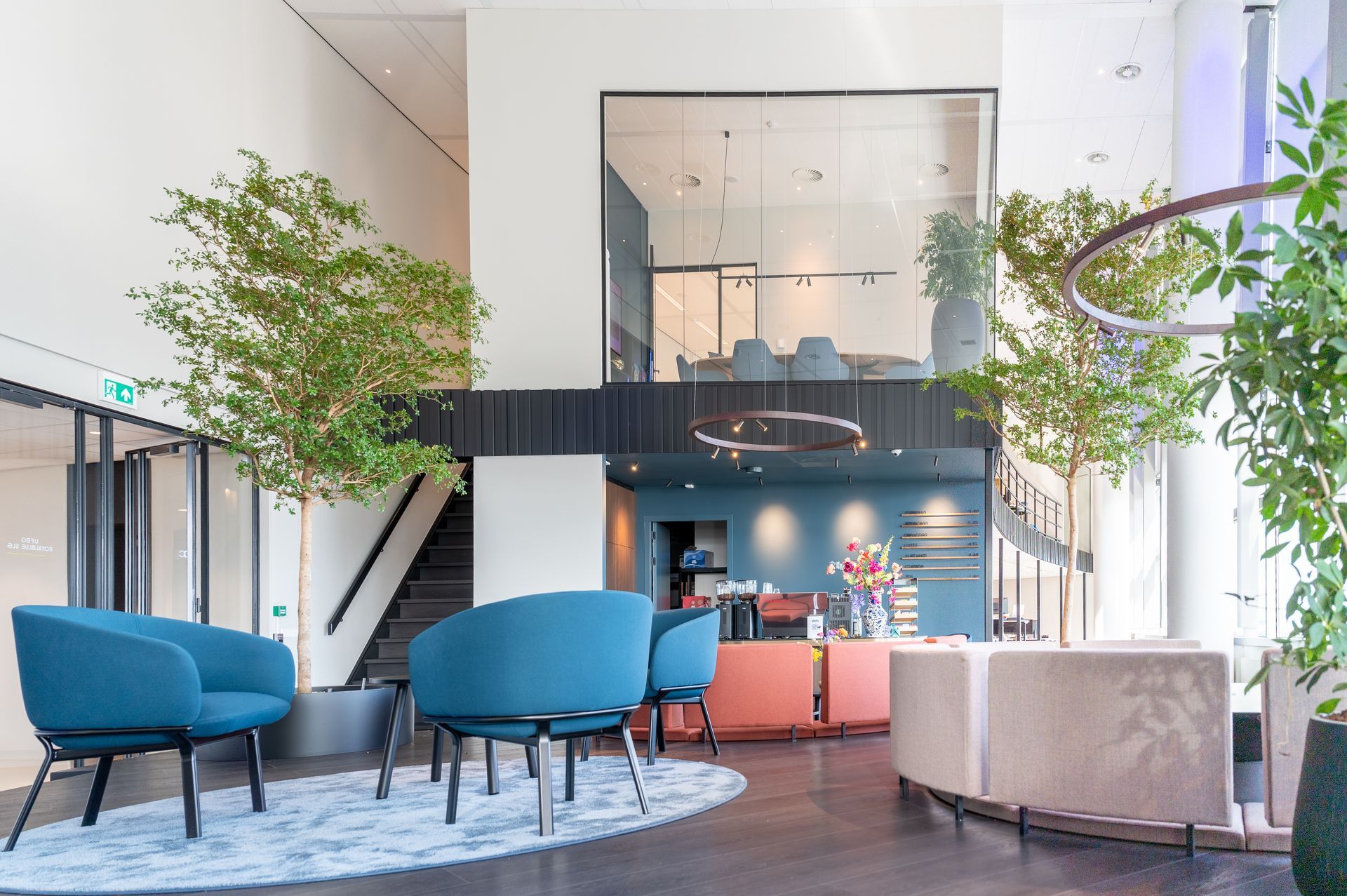 Moderne lobby met blauwe stoelen, roze banken, kamerplanten en een grote mezzanine met ramen.