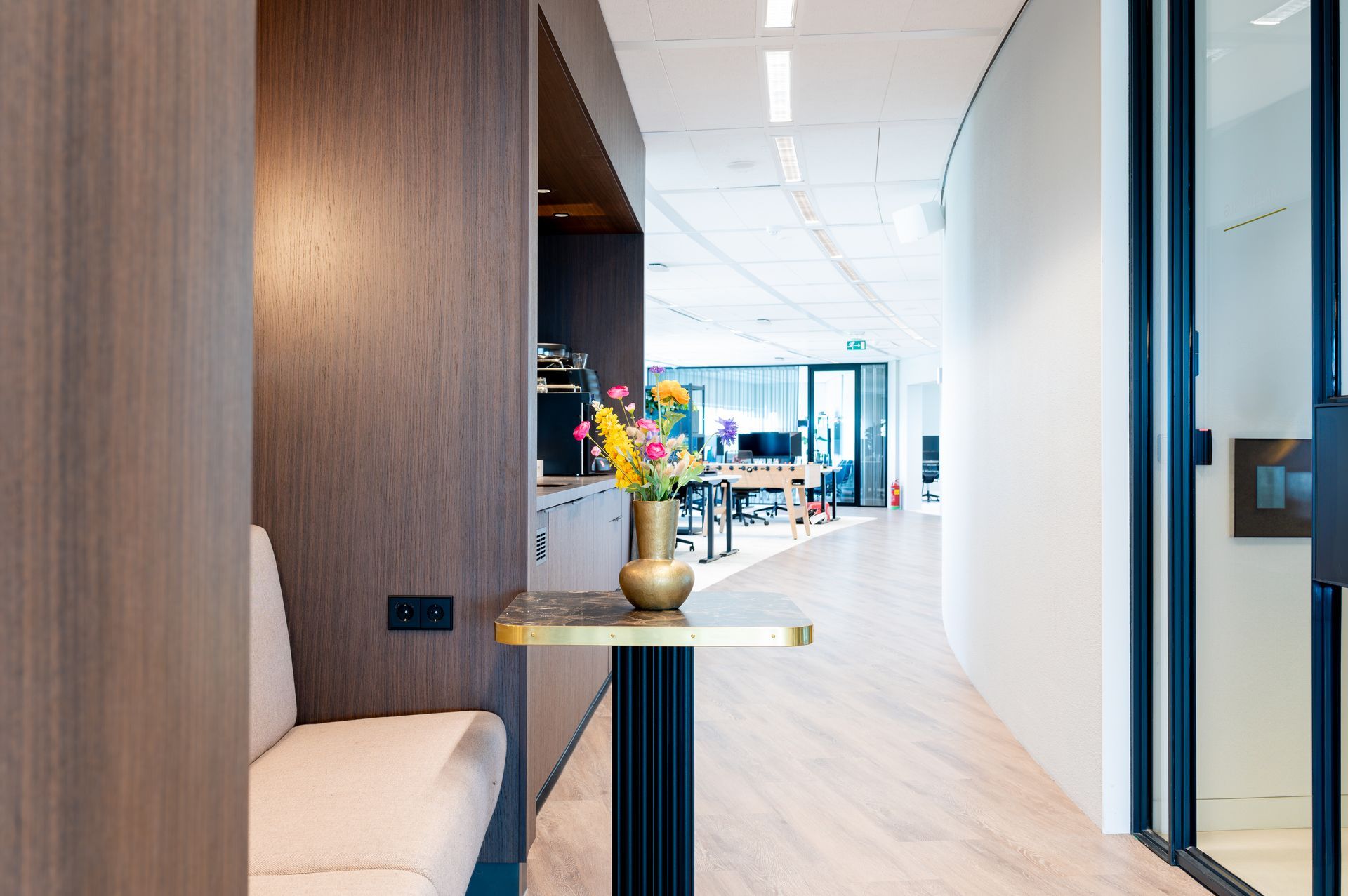 Moderne kantoorhal met een zithoekje bekleed met houten lambrisering en een vaas met bloemen op een tafeltje.