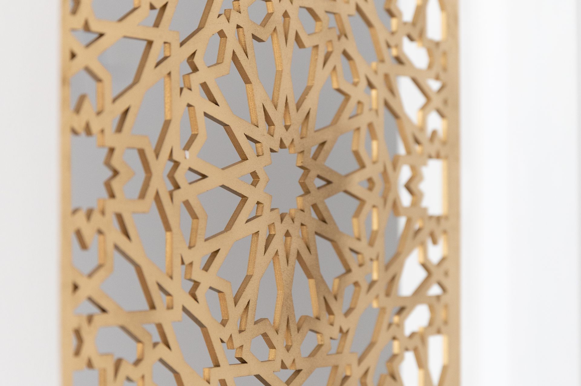 Detailopname van een beige wandpaneel met geometrische uitsnijdingen tegen een witte achtergrond.