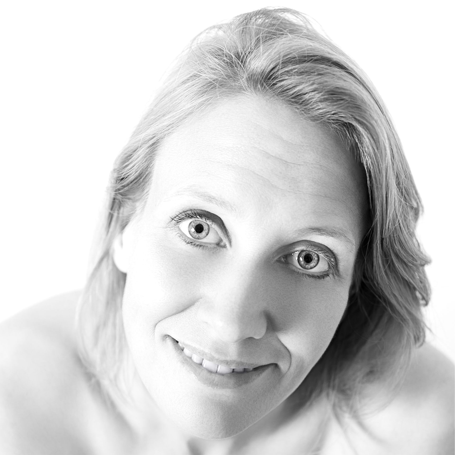 Lachende vrouw met licht haar kijkt omhoog naar de camera in een helder, licht portret.