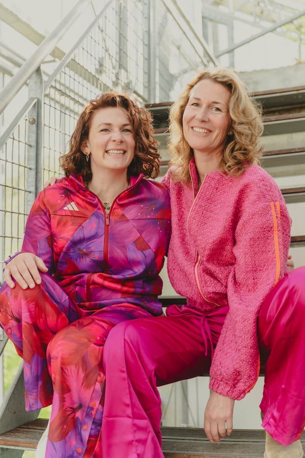 Twee mensen in felroze outfits zitten buiten op een trap en lachen.
