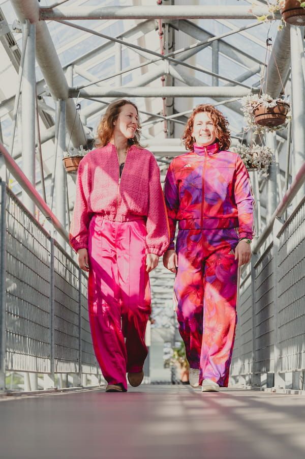 Twee mensen in felroze outfits lopen door een glazen loopbrug.