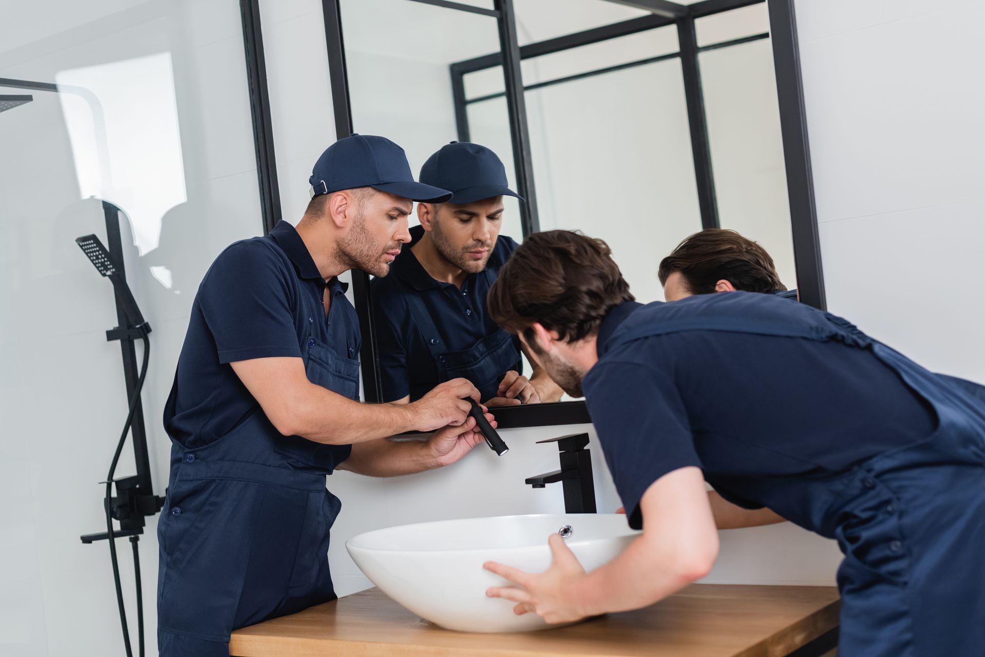 Plumbers checking the sink in a bathroom with a flashlight.