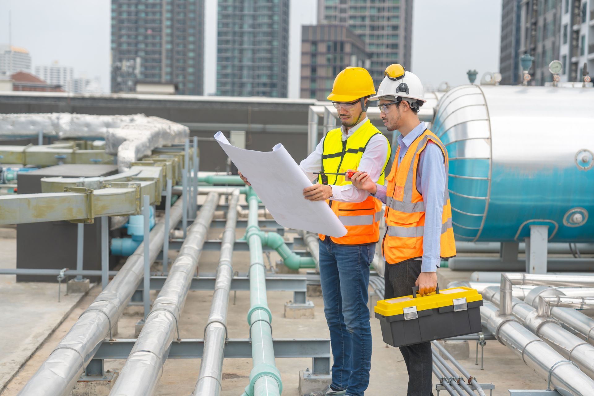 Two commercial plumbers inspecting industrial plumbing plans on a rooftop pipeline system.