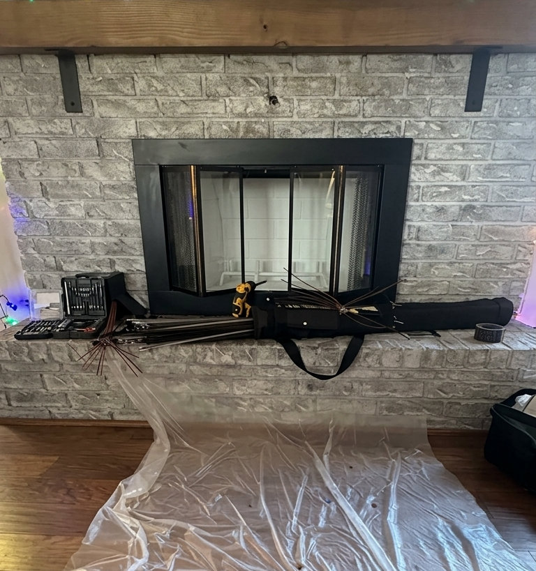 Fireplace with tools and a long black case on the mantel, protective plastic covering the floor.