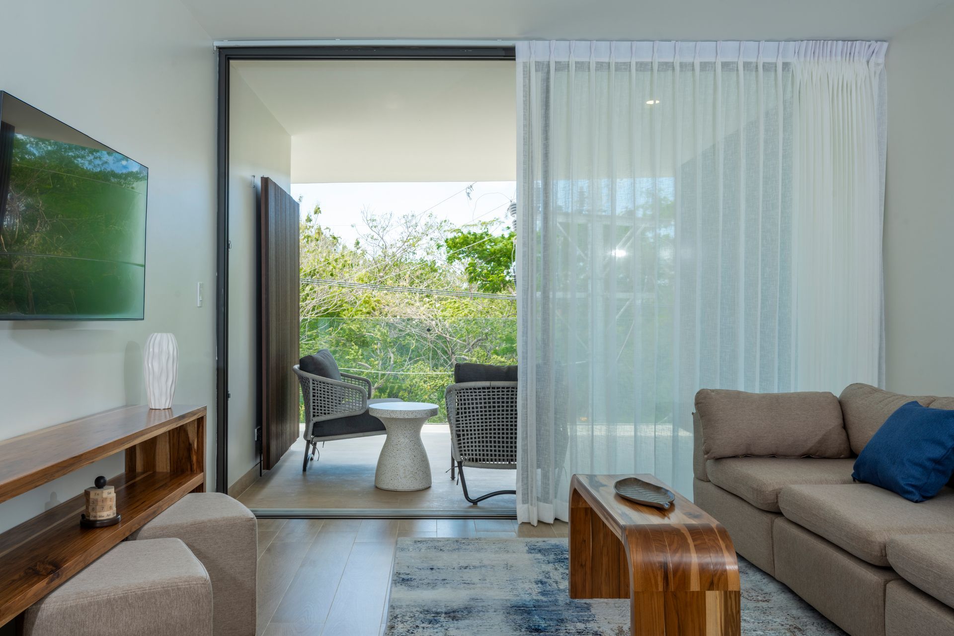Modern living room opening to a bright balcony with plants and sheer curtains
